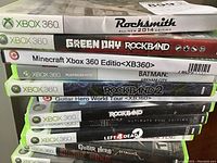 Stack of 11 Xbox 360 game cases showing titles including Rocksmith 2014 Edition, Green Day Rockband, Minecraft, Batman Arkham City, Rockband 2, Guitar Hero World Tour, Rockband Ultimate Evil Edition, Left 4 Dead 2, Guitar Hero Metallica, The Beatles Rockband.