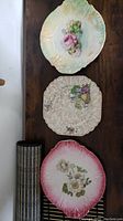 Three decorative plates shown together laid on wooden surface, each with distinct floral designs and pastel color accents