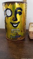 Close up of vintage Planters tin can with yellow/gold color and Mr. Peanut face logo, showing rust and wear.