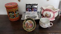 Wide view of lot with Barnum's Animals tin, two Le Hockey Legends figurines, two decorative plates, ceramic teacup, and pink floral vase on wooden surface.