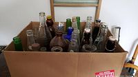 Top view of cardboard box filled with about 20 old glass bottles in clear, brown, green, and blue glass.