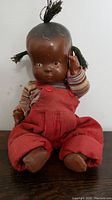 Front view of vintage baby doll with yarn hair, striped shirt, and red corduroy overalls.