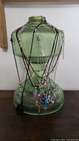 Lot of multiple necklaces exhibited on a green glass lantern base, chains and cords visible featuring various pendants including key heart and crescent moon.
