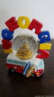 Front view of VW snow globe showing red and white VW van with surfboards and SoCal arch letters around the globe containing a sandcastle