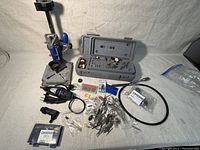 Photo showing the Dremel 300 rotary tool, drill press stand, flexible shaft, and various bits and accessories spread on a table.
