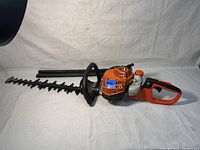 Side view of orange and black ECHO HC-2020 gas hedge trimmer with blade cover.