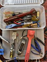 Plastic bin with assorted hand tools including pipe wrench, screwdrivers, pliers, pry bar, and handles