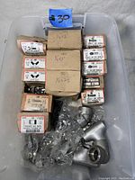 Plastic container with boxes and bags of new stainless steel hardware, including hex cap screws, wing nuts, cotter pins, finished hex nuts, and socket cap screws.