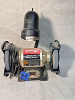Front view of RYOBI 6" Thin Line Bench Grinder showing grinding wheels, protective guards, lamp, and power switch.