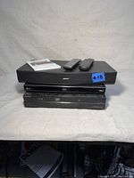 Stack of three electronics: BOSE Solo TV Soundbar on top, LG Blu-ray player middle, Sony RDR-VXD655 VHS/DVD player bottom. Two remotes and manual on top.