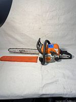Full side view of chainsaw with guide bar installed and scabbard laid next to it