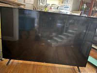 Front view of the 55 inch TCL TV showing the full screen and frame with two supporting legs spaced wide apart beneath the TV. The screen is off and reflective.