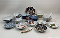 Multiple Asian kitchen ceramic pieces arranged on white background. Includes various bowls, plates, dipping dishes, chopstick rest, and ceramic spoons.