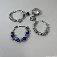 Three charm bracelets along with a silver-tone ring and two decorative round charms with filigree details on a white background.
