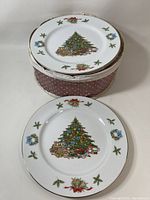Set of 11 Christmas plates stacked, showing the decorated Christmas tree plate on top and fabric case beneath