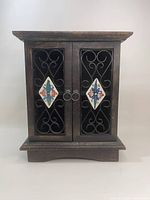 Front view of dark wood cabinet with two doors featuring iron grills and colorful ceramic tiles