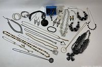 Overview of assorted jewelry including necklaces, earrings, and bracelets arranged on white surface with small plastic tote visible in background