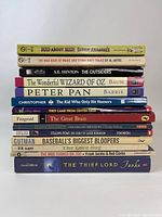 Stack of 13 paperback books with visible titles showing a variety of genres including comics, classic literature, and sports.