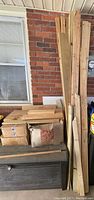 Photo showing stacked spare wooden studs and boards leaning vertically against a brick wall, various lengths are visible.