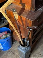 Tall metal vase holding three unique walking canes, showing condition and details of each cane.