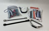Overview of two Fitbit devices, multiple colorful replacement bands in two mesh bags, and three metal mesh bands arranged on a white surface.