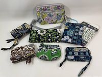 Nine Vera Bradley textile accessories including wallets, wristlets, pouches, and a floral fanny pack laid out on a white surface.