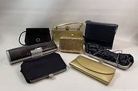 Front view of 7 vintage handbags and wallets in black and gold tones arranged on white background.