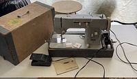 Pfaff sewing machine setup on table with hard carrying case, foot pedal, and instruction manual visible.