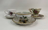 Four vintage teacups and saucers with floral patterns and gold accents arranged for display.