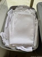 White chair covers folded and placed inside a beige plastic Sterilite storage bin, showing condition and quantity approximate.