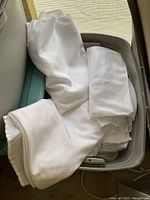 White linen folded tablecloths mostly round, with some rectangular, in gray plastic Sterilite tote container.