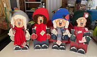 Photo showing all four wooden Christmas caroler figurines side by side, displaying different colored hats, scarves, and wooden bases.