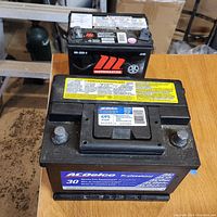 Two black car batteries side by side: ACDelco Professional 47PS (large) and MotoMaster (small).