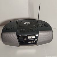 Front view of JVC portable CD player showing control buttons, speaker grills, and antenna.