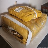 Yellow electric heated blanket in clear plastic zippered bag, with matching electric massage pillow on top, both showing cords and plugs.