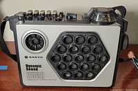 Front view showing silver panel with large speaker grills, small round speaker, and brand markings