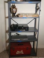 Front and angled view of the grey steel shelving unit with various items on shelves for scale only, against a white wall.
