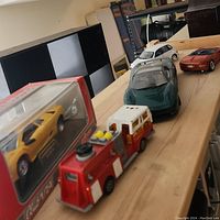 Photo showing 5 vintage model cars displayed in a row on a wooden surface, including one boxed yellow sports car and visible fire truck at front.