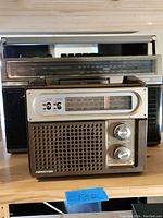 Two vintage radios stacked, smaller radio in front showing front tuning and volume knobs and AM/FM frequency display with switches