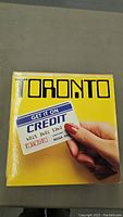 Front cover of Toronto album 'Get It On Credit' with yellow background and image of hand holding credit card.
