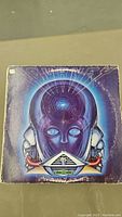 Front cover of Journey's 'Frontiers' vinyl album showing a blue robotic head with an illuminated circular center on the forehead, worn corners.