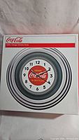 Box front showing the vintage style chrome clock with Coca Cola branding and markings.