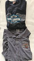 Black Harley Davidson t-shirt and grey Harley Davidson polo shirt folded showing logos and colors.
