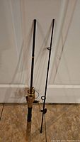 Three black and gold fishing rods with spinning reels, shown standing upright against a door, displaying the full length and handle detail.