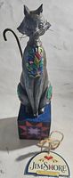 Full view of the carved gray cat figurine with colorful floral painting on chest sitting on a painted square base with quilt star design.