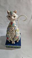 Front view of white cat figurine showing colorful floral patterns and detailed face with whiskers.