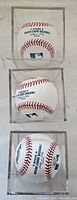 Three official Major League Baseballs stacked vertically, each in its own clear plastic display case showing red stitching and printed MLB logos.