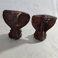 Two hand carved wood cobra statues standing side by side showing front and side details