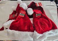 Photo showing multiple new red and white Santa hats, assorted sizes, with original tags attached.