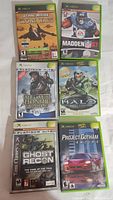 Six original Xbox game cases displayed together on a fabric surface.